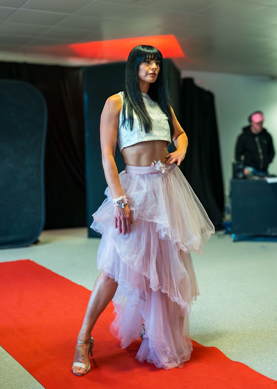 Model walks the runway wearing a flowing pink tulle skirt and white top during a fashion show event.