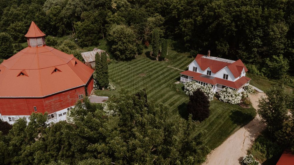 Aerial view of a rustic wedding venue with red roofs nestled among lush green trees and landscaping.