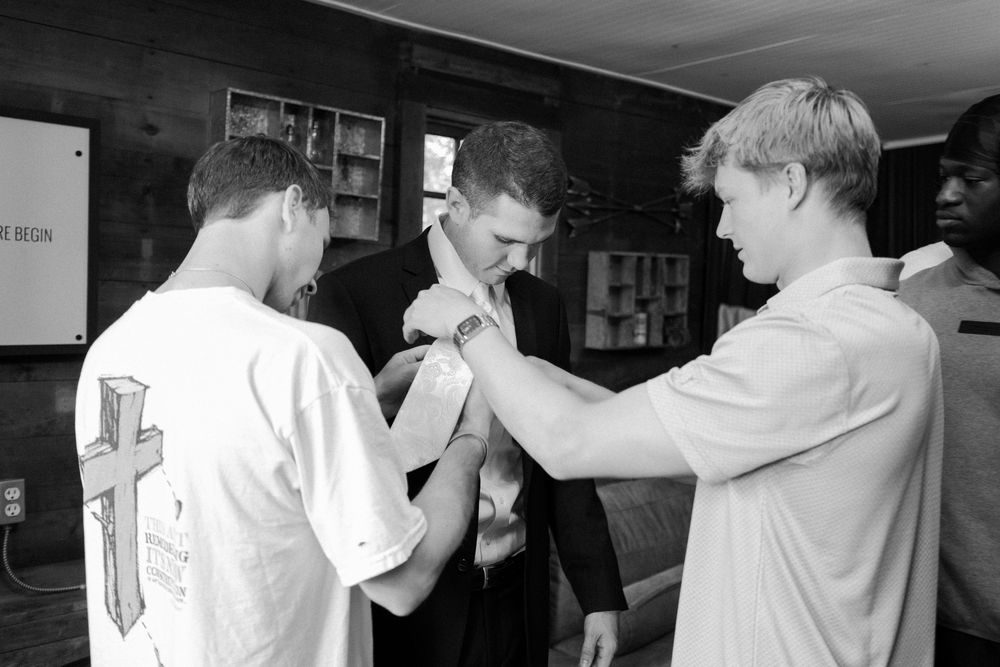 Black and white photo of groomsmen getting ready in a casual setting.
