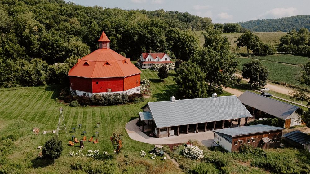 Aerial view of a wedding venue complex with red barns and buildings surrounded by green countryside.