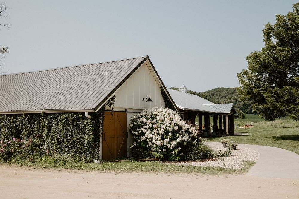 Rural farm buildings and barns line a gravel path surrounded by green landscaping.