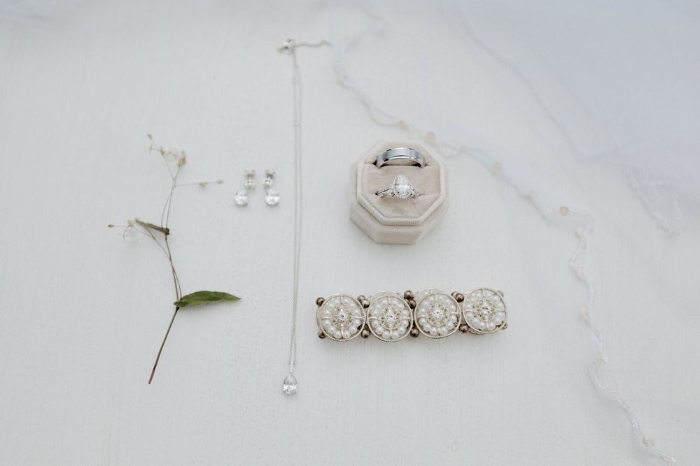 Wedding rings and delicate jewelry details arranged on white marble surface.
