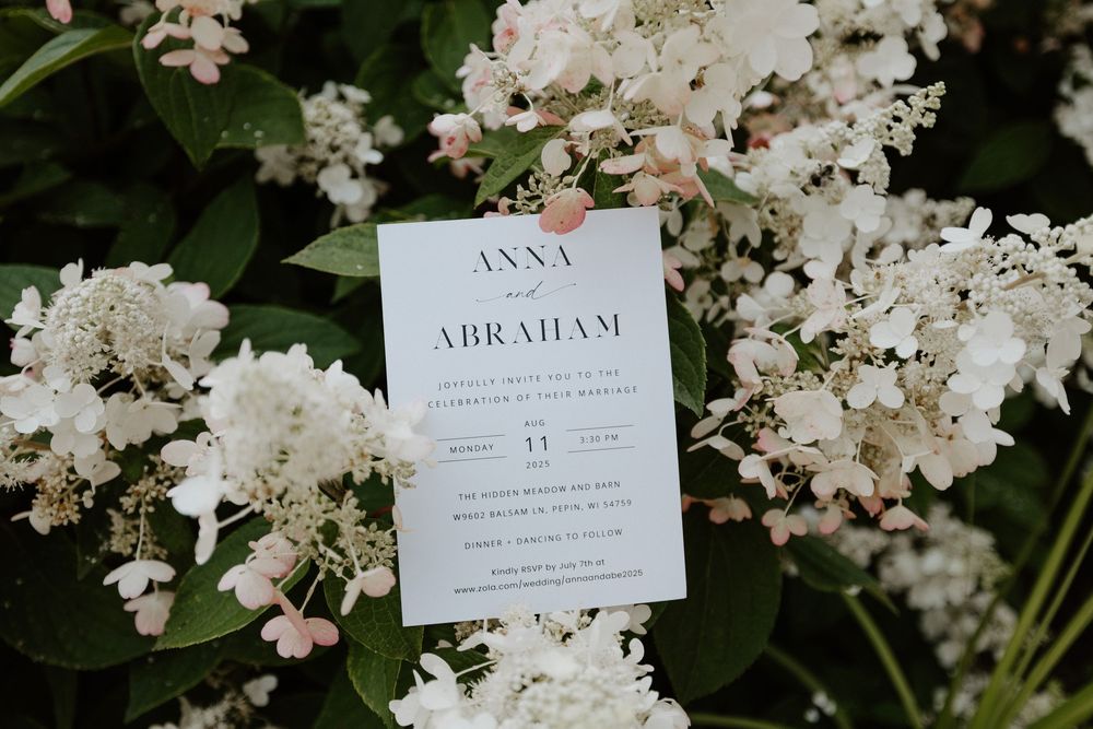 Elegant white wedding invitations displayed among delicate white floral blooms and greenery.