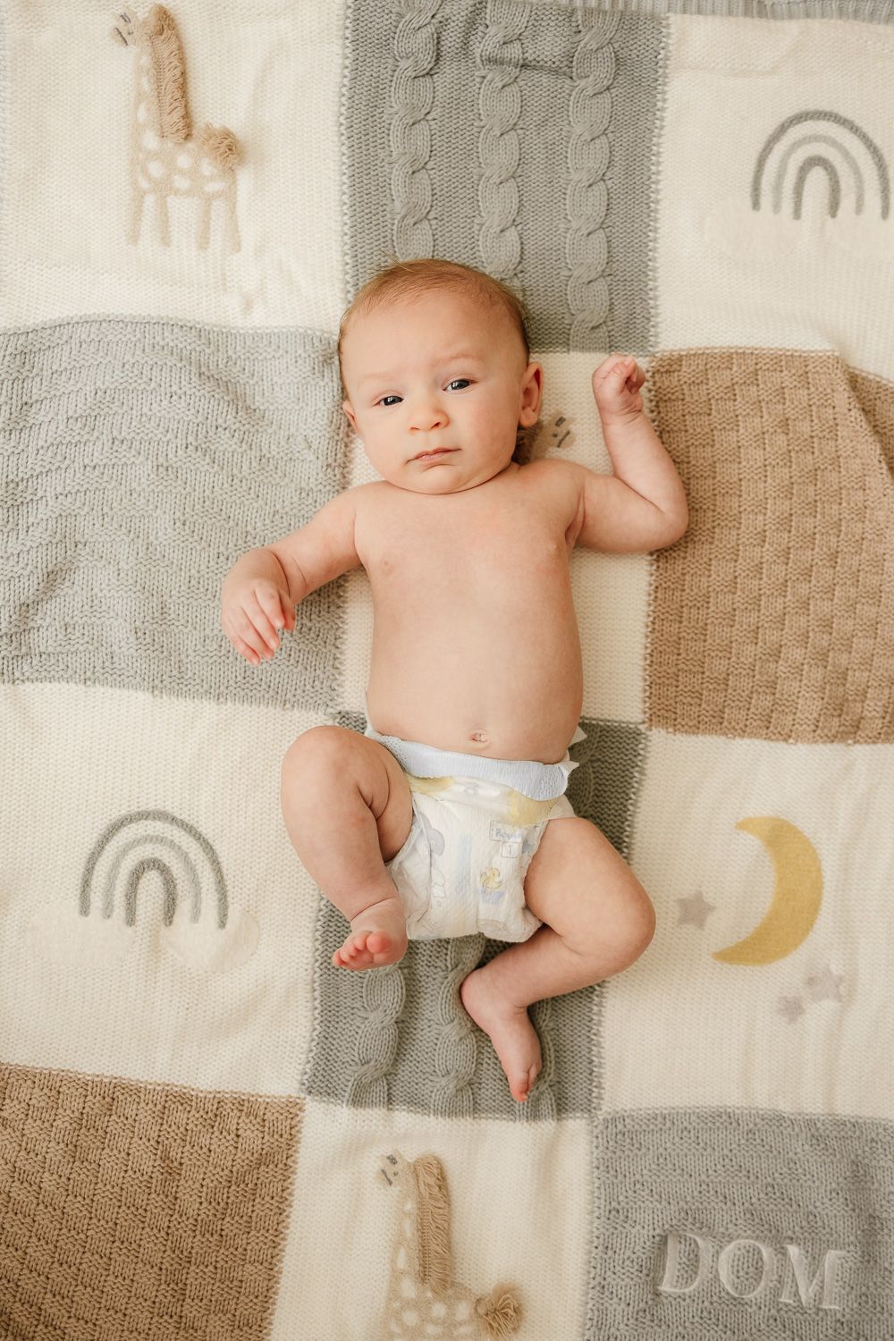 A baby lays on his blanket looking into the camera