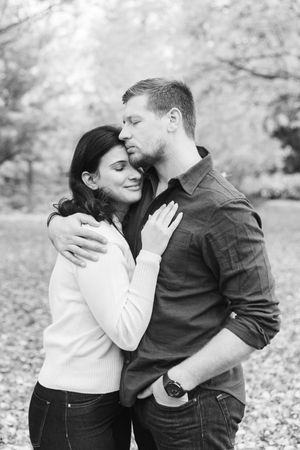 Black and white photo series of a romantic couple embracing and laughing together in an autumn setting with fallen leaves.