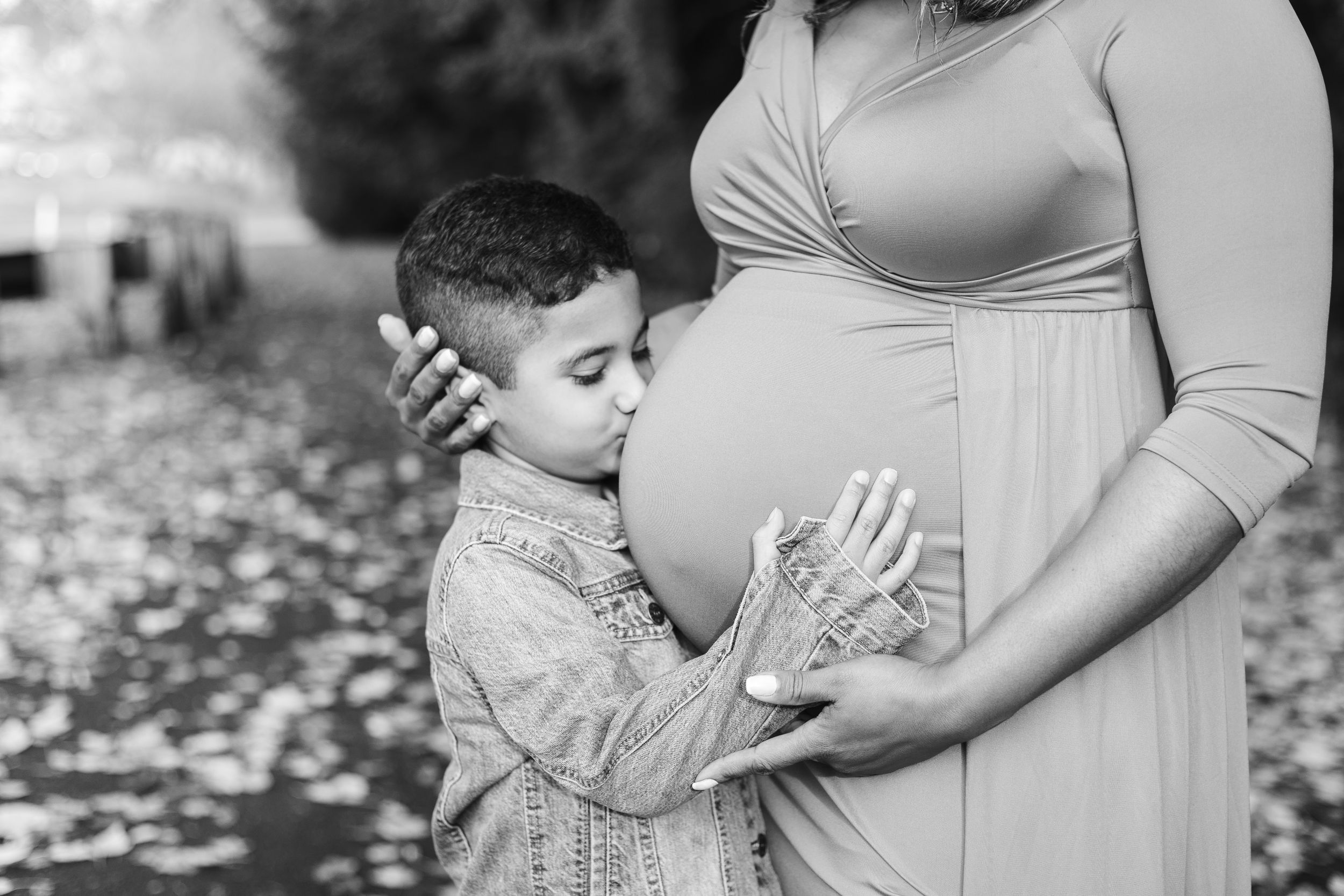 A pregnant woman in a light dress holds her belly while standing outdoors during a maternity photo session.