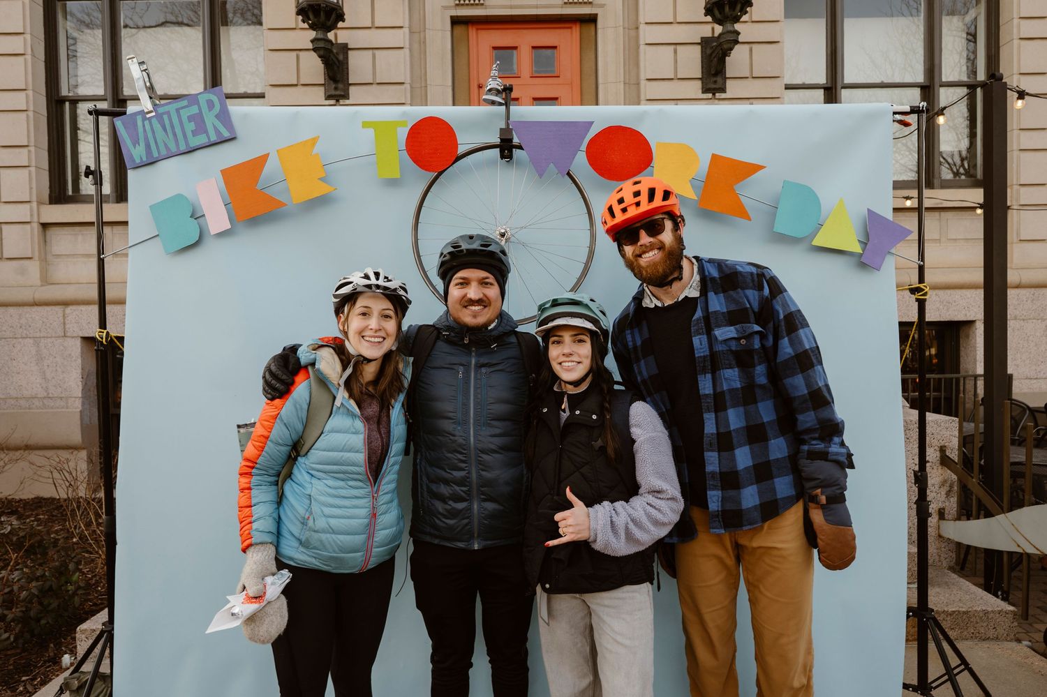 A group of cyclists in winter clothing and bike helmets pose together on urban steps for a group photo.