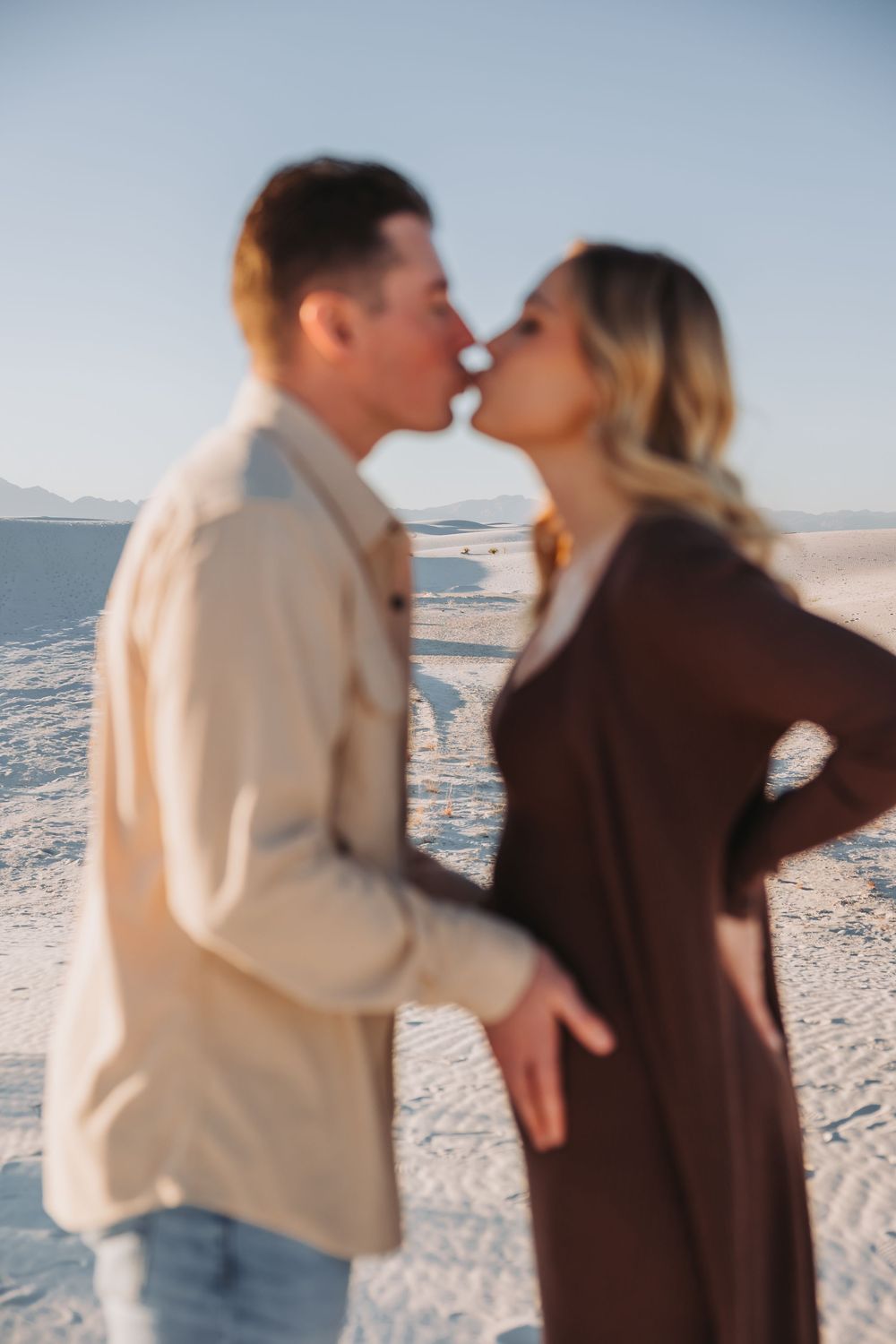 A couple shares a romantic moment on a sandy beach during sunset with ocean waves in the background.