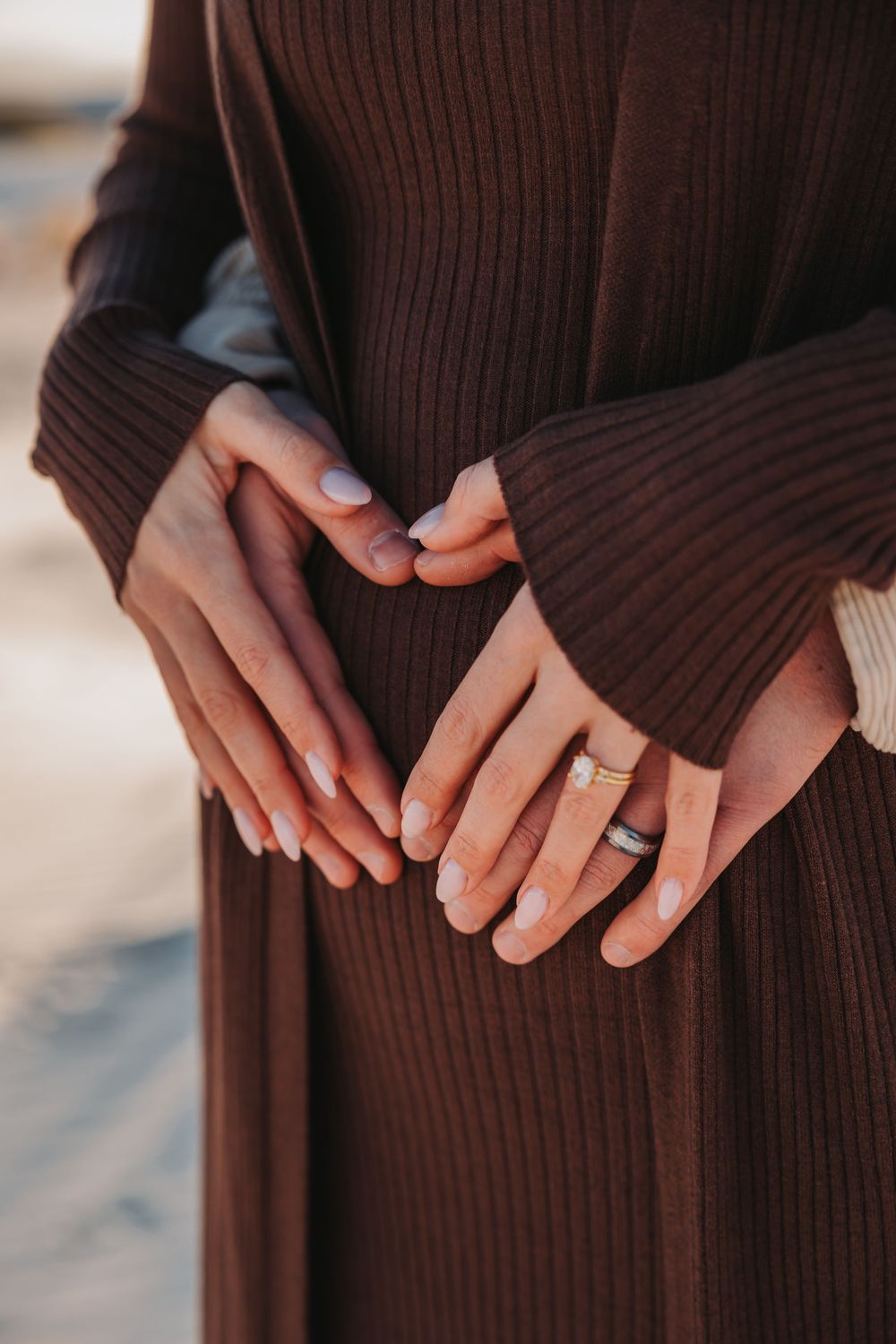 Close-up view of hands wearing a gold wedding ring against a dark brown ribbed sweater or dress fabric.