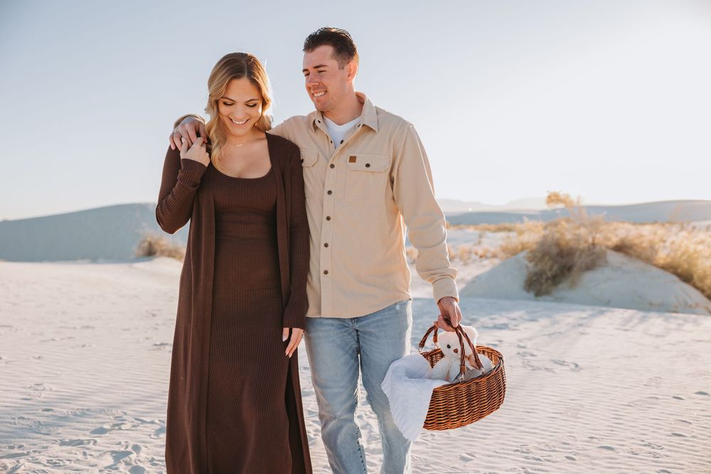 A couple walks together on a sandy beach at sunset wearing brown and beige casual clothing.