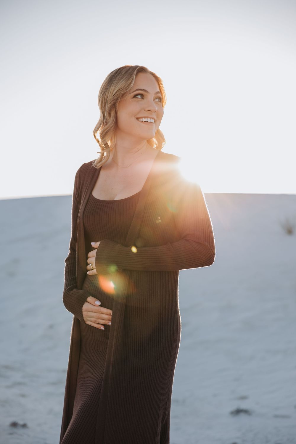 A person in a black sweater laughs joyfully against a bright sunlit background creating a warm backlit glow.
