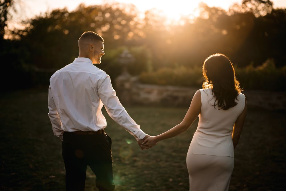 Silhouetted couple holds hands against warm sunset light in garden setting.