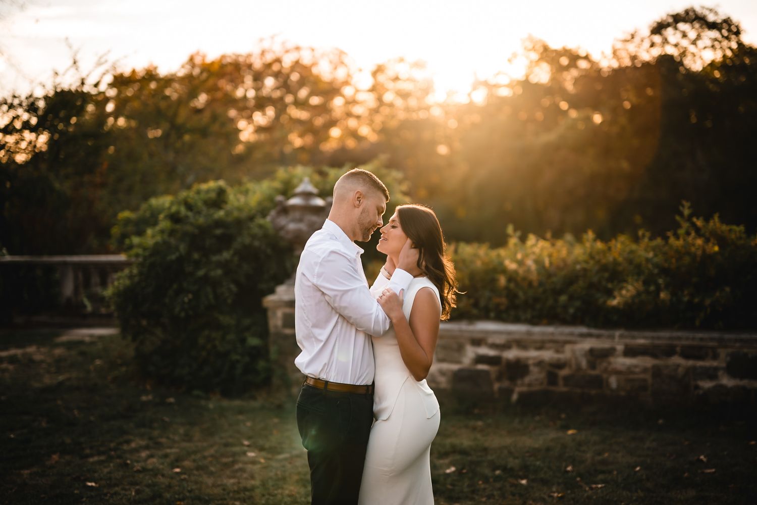 Romantic couple embraces during golden hour sunset in an outdoor garden setting.