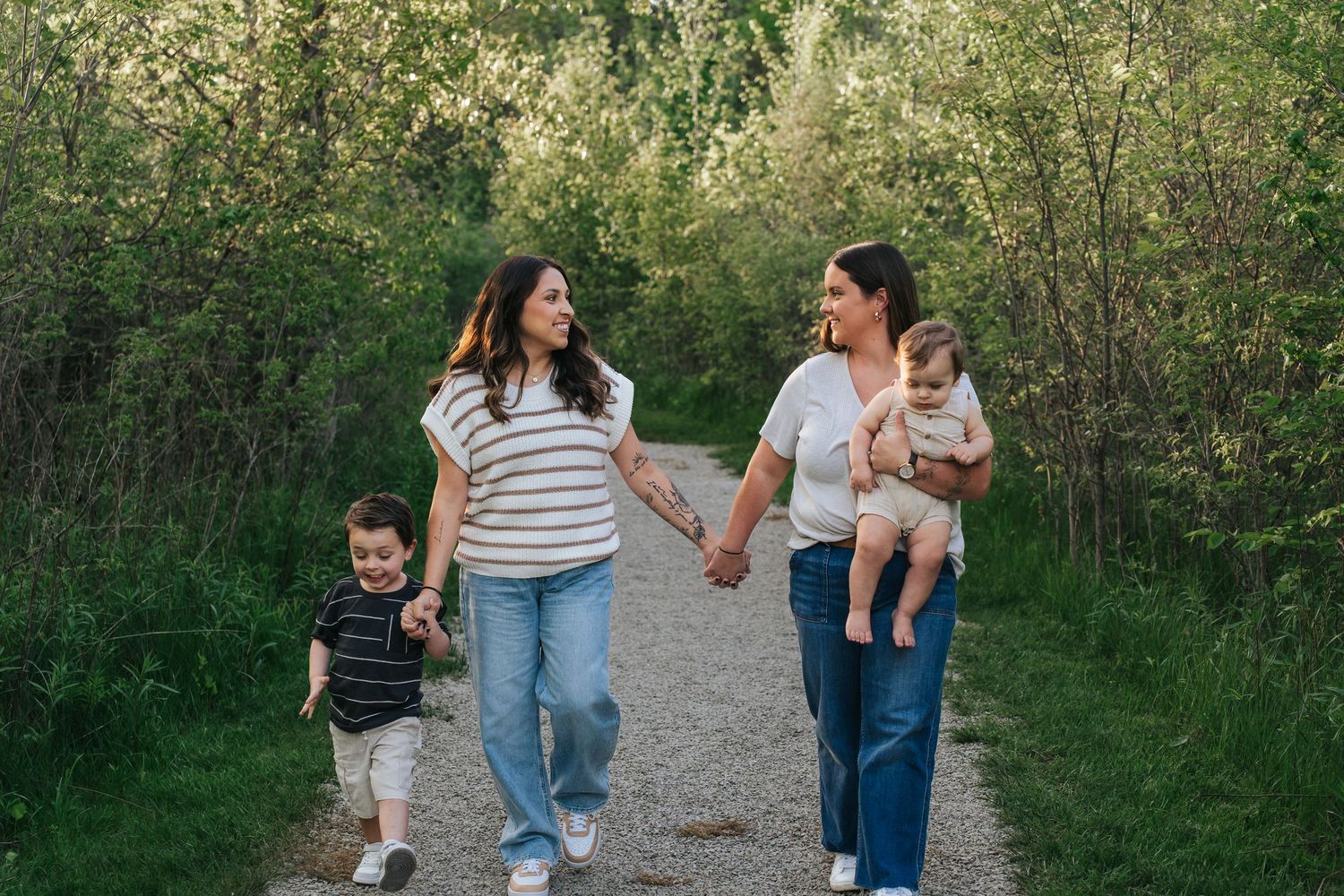 Family walking together on a tree-lined nature path during a sunny afternoon.