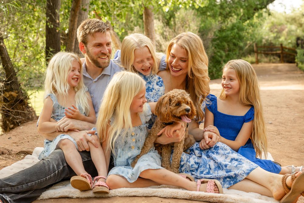 a couple with 4 young girls laughing together sitting on a blanket wooded area in southern utah