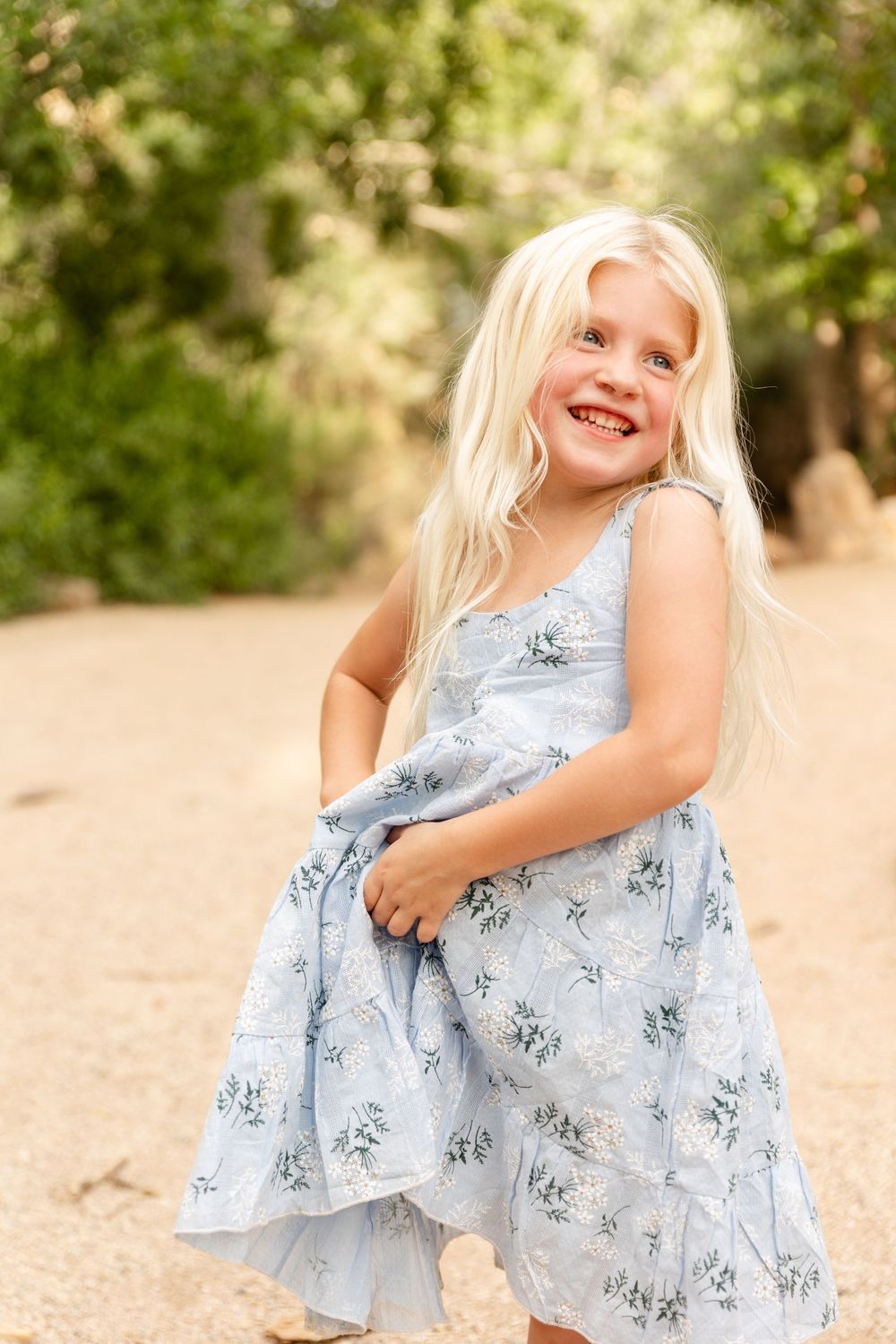 a young blonde girl holding her pretty blue dress laughing off camera