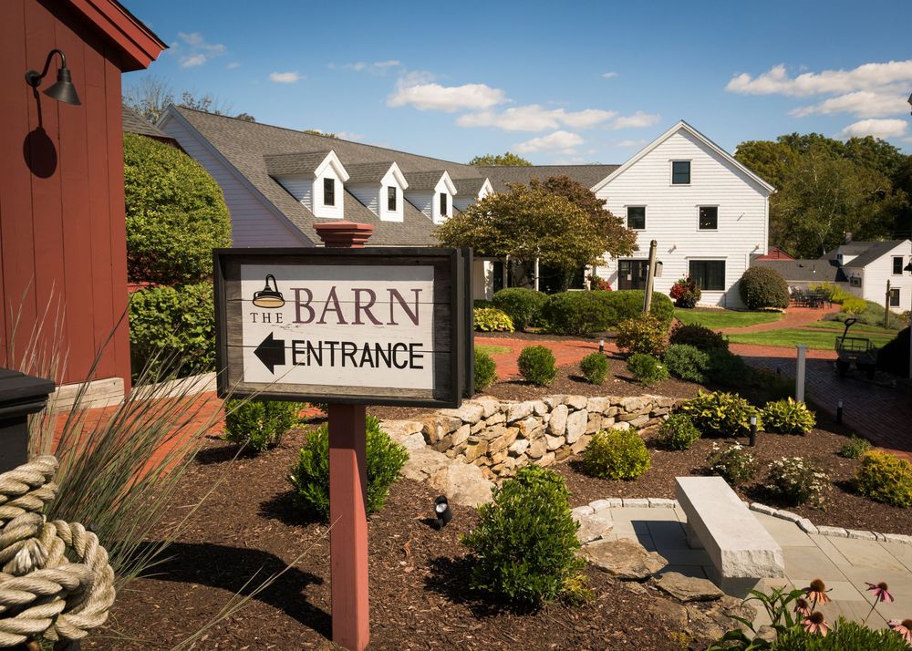 Landscaped entrance pathway to barn venue with directional signs and rock gardens under blue sky.