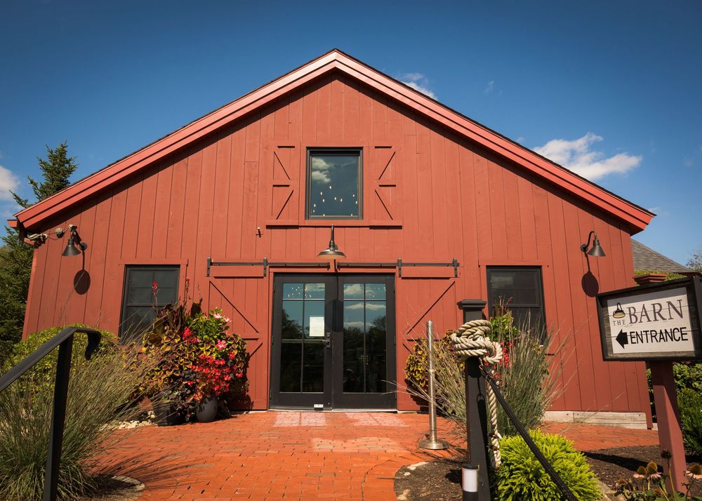 Panoramic view of a rustic red barn venue with white trim and surrounding greenery on a sunny day.