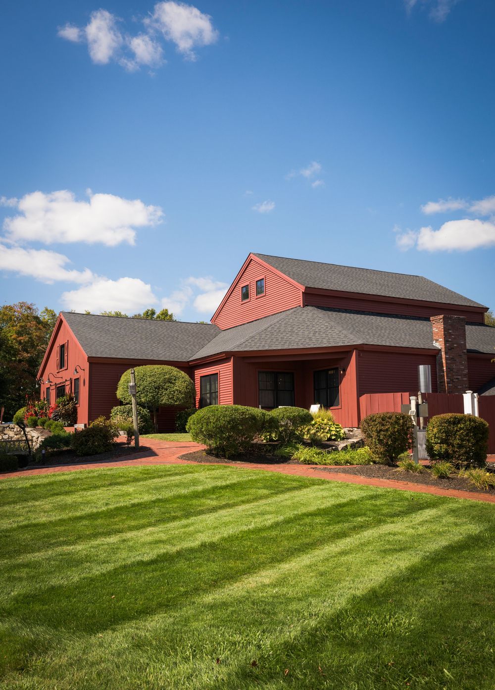 A large red barn-style building with striped lawn and landscaping under a bright blue sky with white clouds.