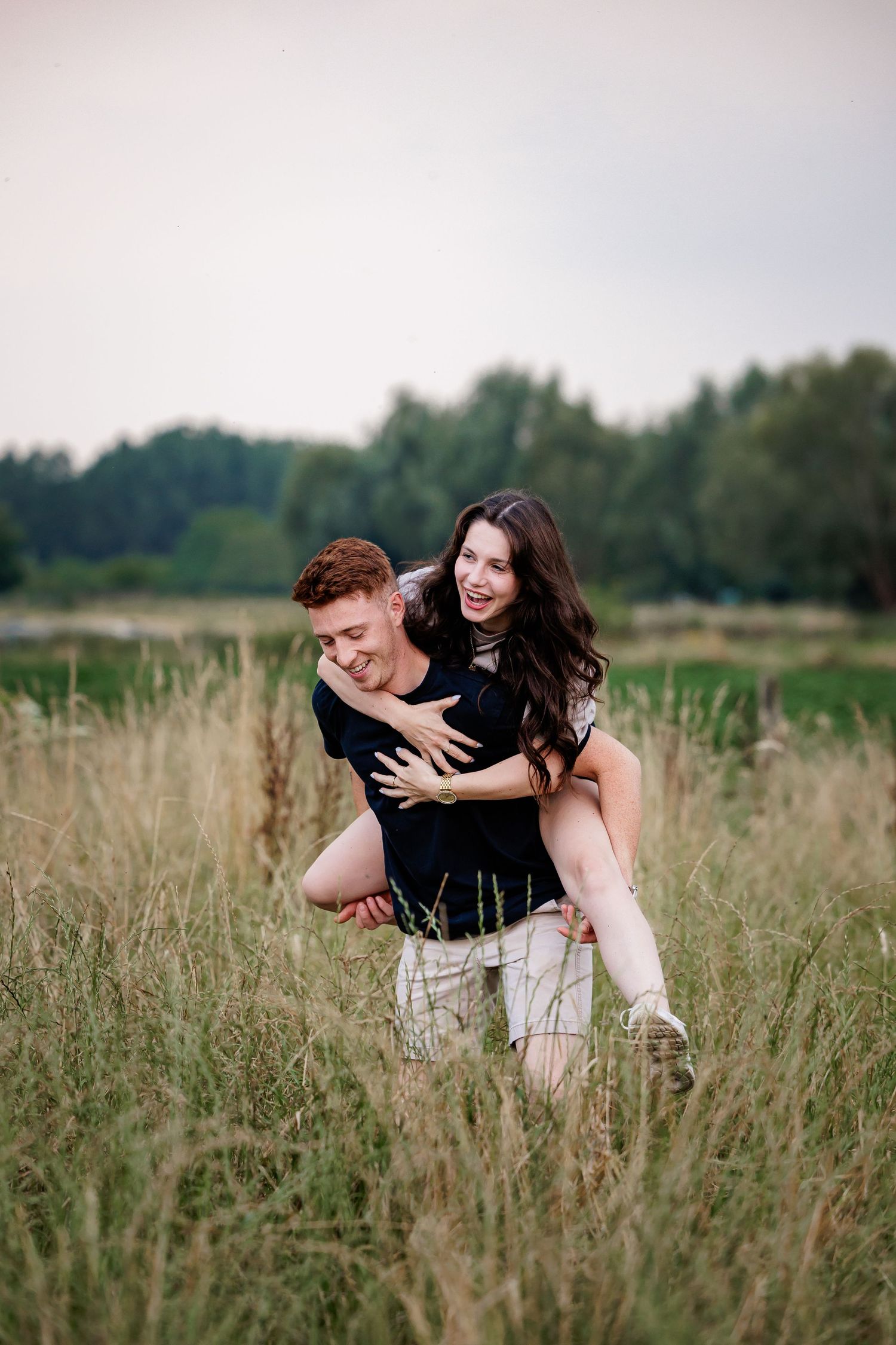 A couple embraces playfully in a field of tall grass on a summer afternoon.