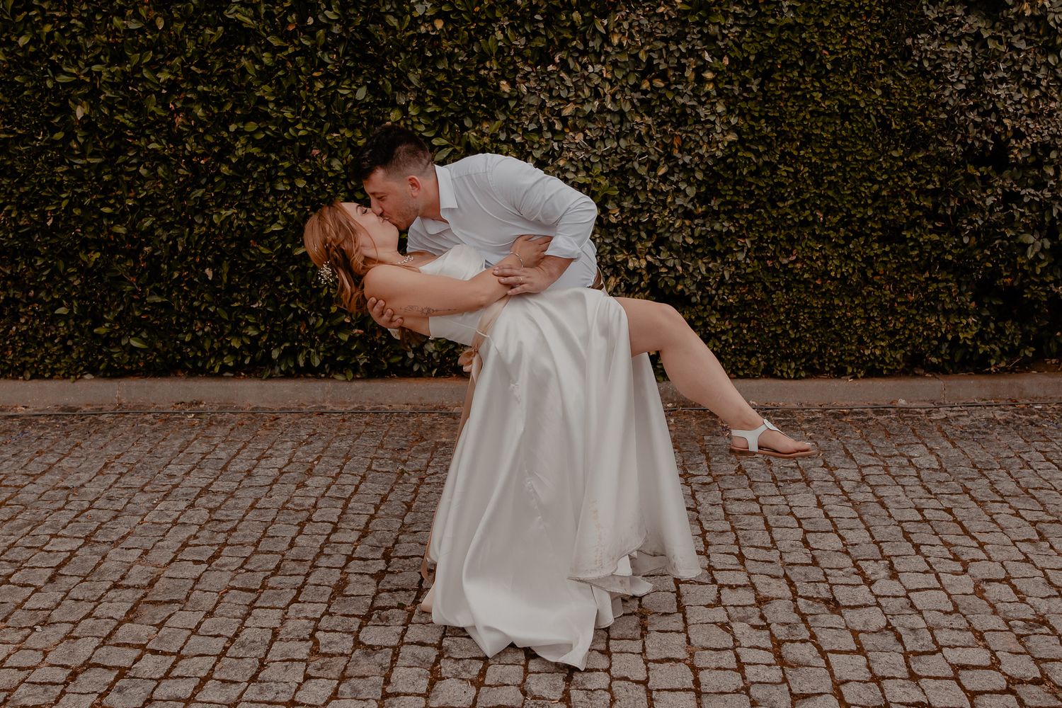 Couple dancing on cobblestone path with flowing white dress in motion.