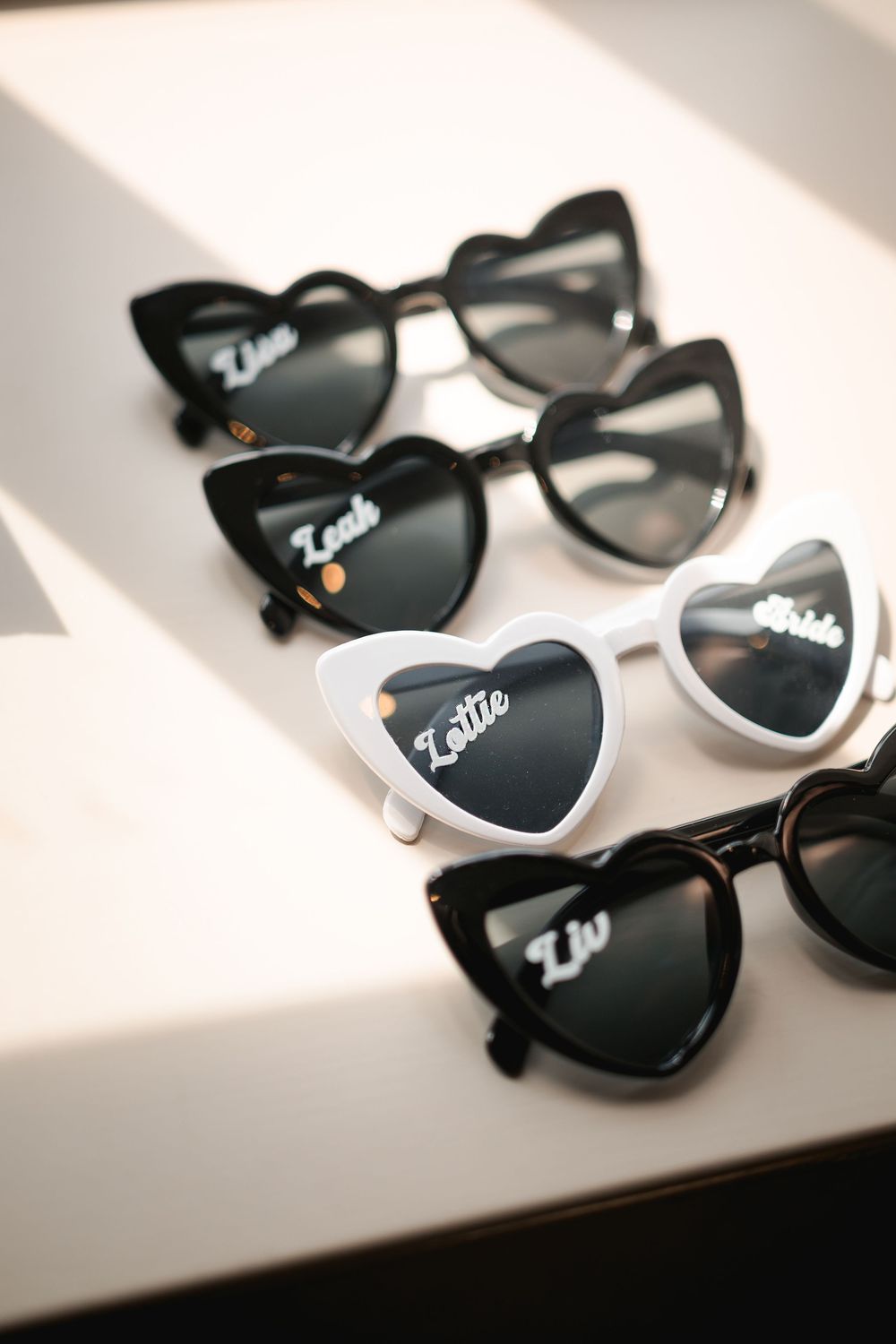 Heart-shaped sunglasses arranged in a line casting dramatic shadows on a white surface.