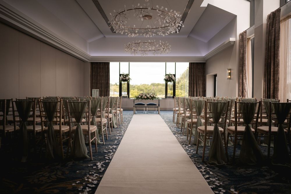 Empty wedding ceremony venue with rows of chairs and an aisle runner leading to a bright window.