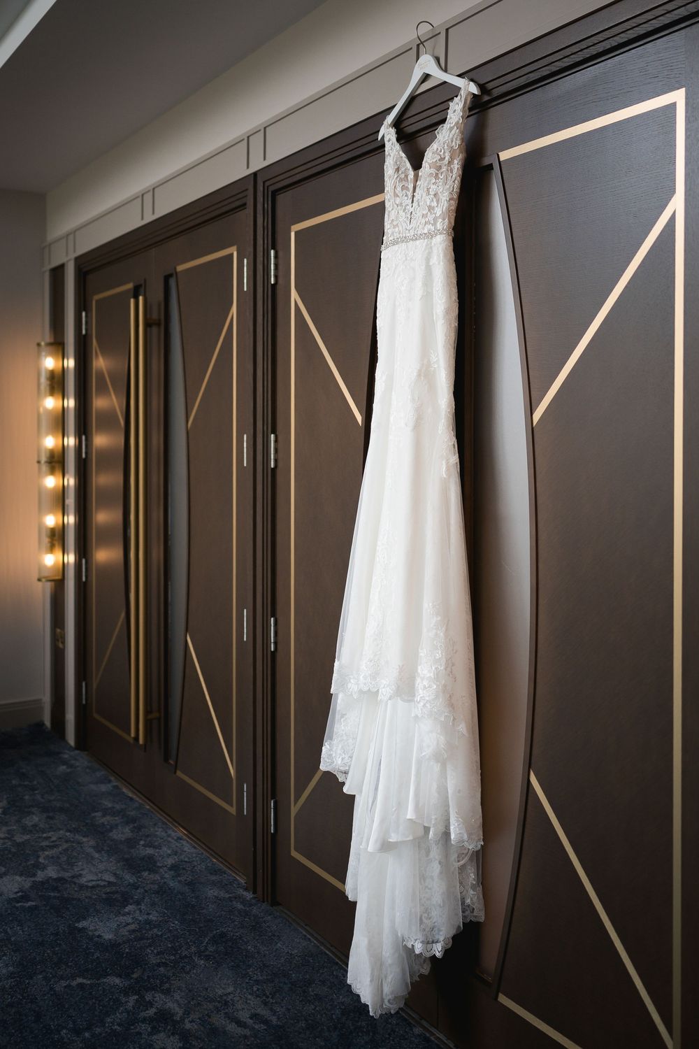 Wedding dress hanging on dark geometric patterned hotel door with modern gold accents.