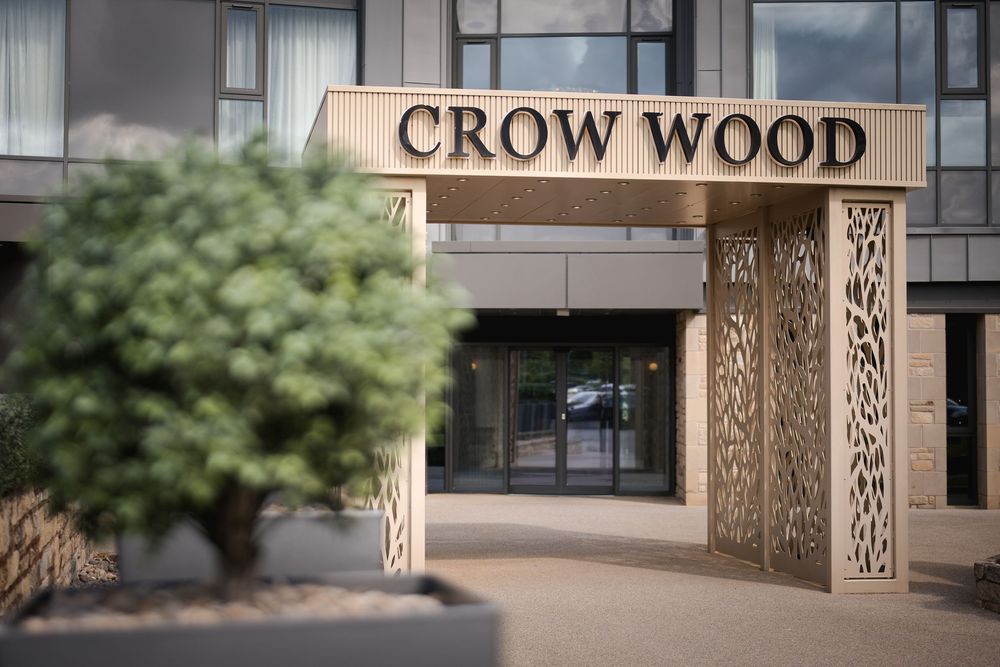 Modern building entrance with brown lettering reading 'CROW WOOD' on a stone wall exterior.