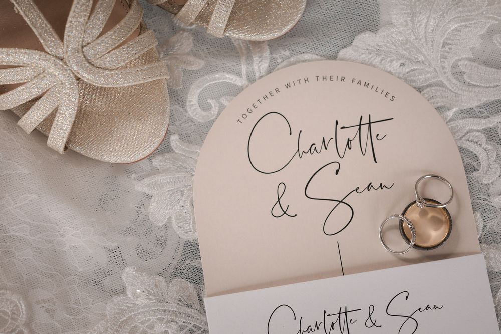 Close-up of wedding invitation cards and rings arranged on white lace fabric with romantic styling.