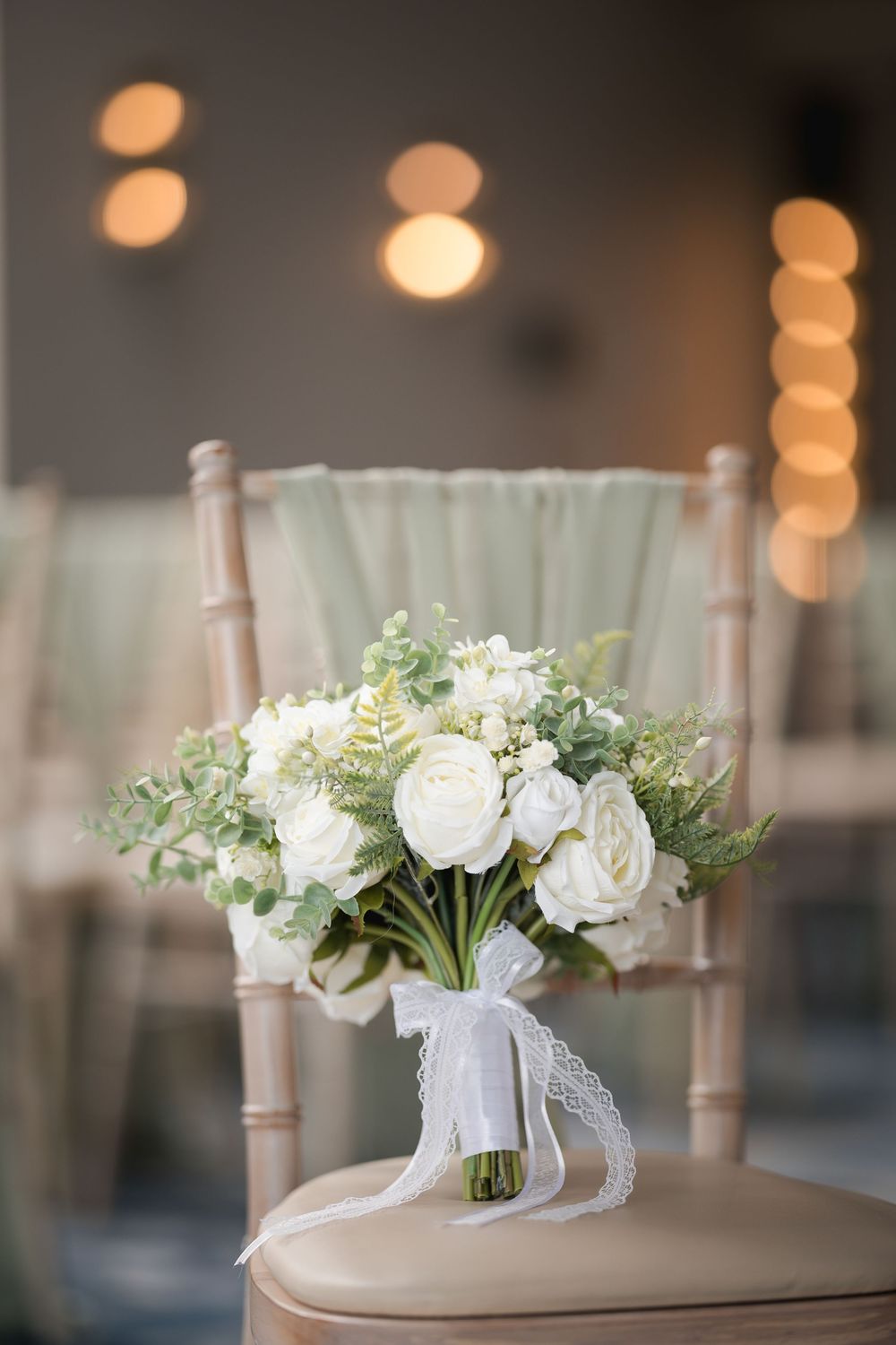 White floral bouquet with delicate ribbons and greenery arranged elegantly against a soft bokeh background.