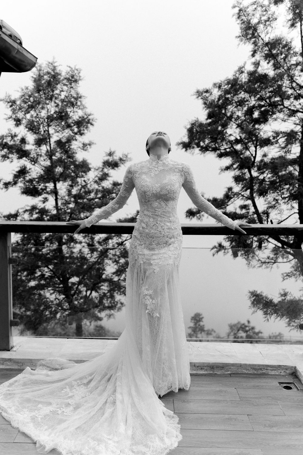 Elegant lace wedding dress with flowing sheer train displayed on wooden deck with mountain backdrop.