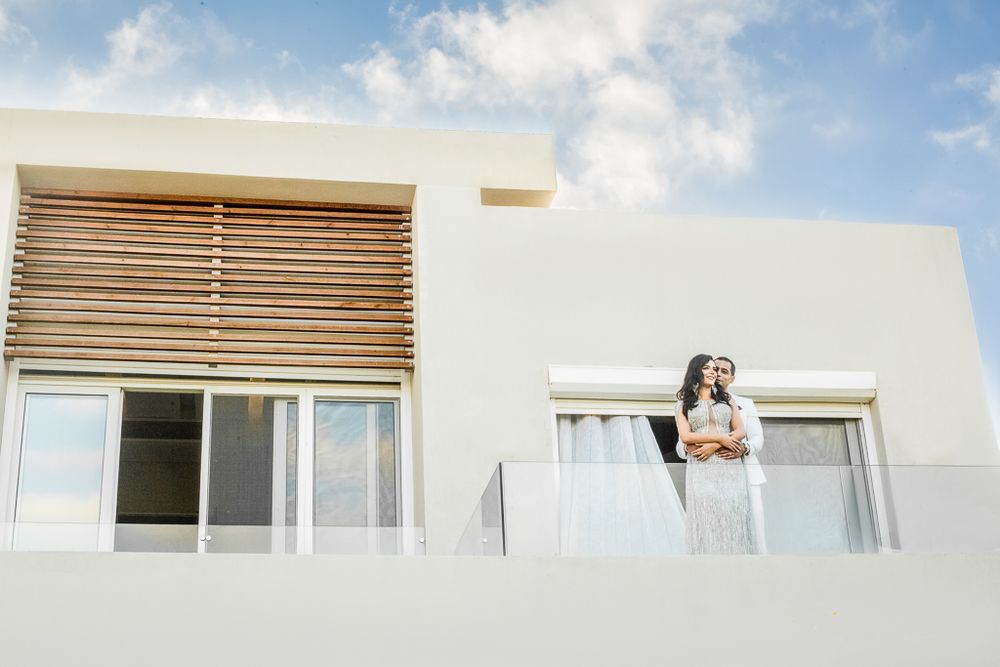 A couple stands together on a modern white balcony against a bright sky.