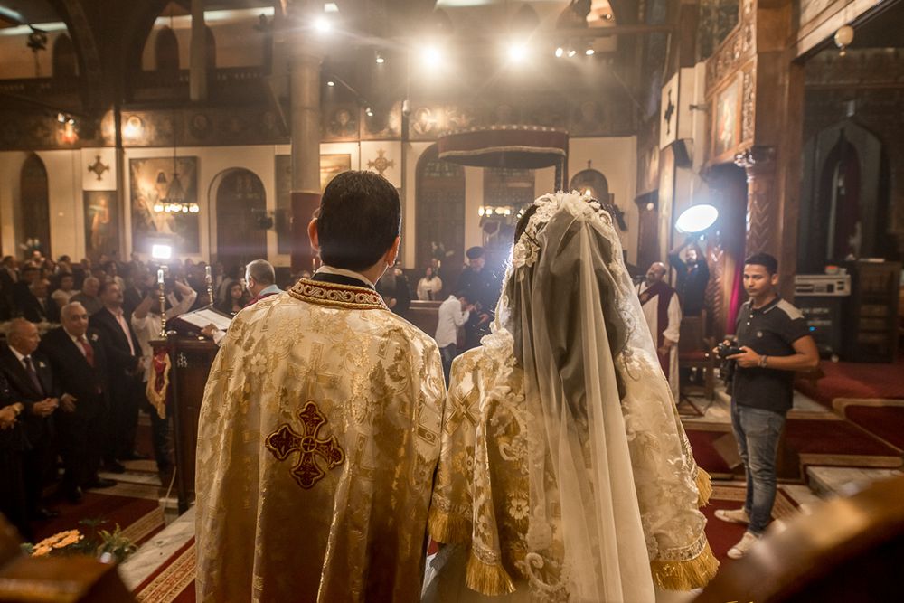 Orthodox wedding ceremony in progress with priest and couple illuminated by church lighting.
