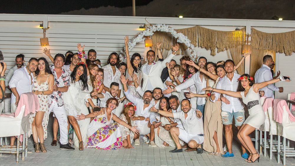 Large group celebrates at festive party with decorative white and pink theme.