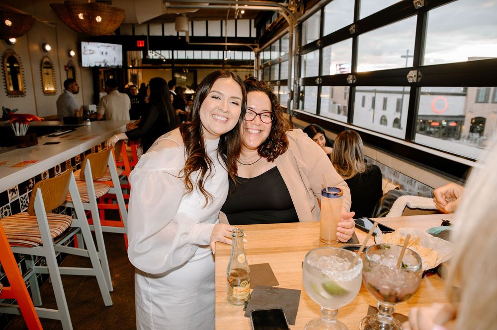 A group enjoys drinks and food while socializing in a restaurant bar area with warm lighting and wooden tables.
