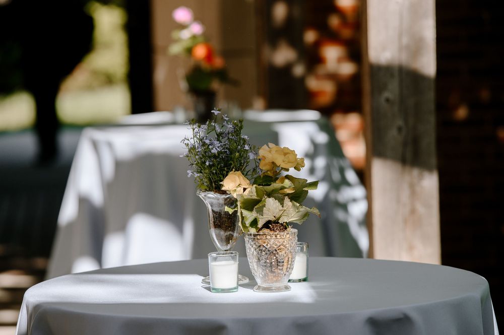 Elegantly decorated wedding reception tables with white linens and floral centerpieces in a sunlit venue.