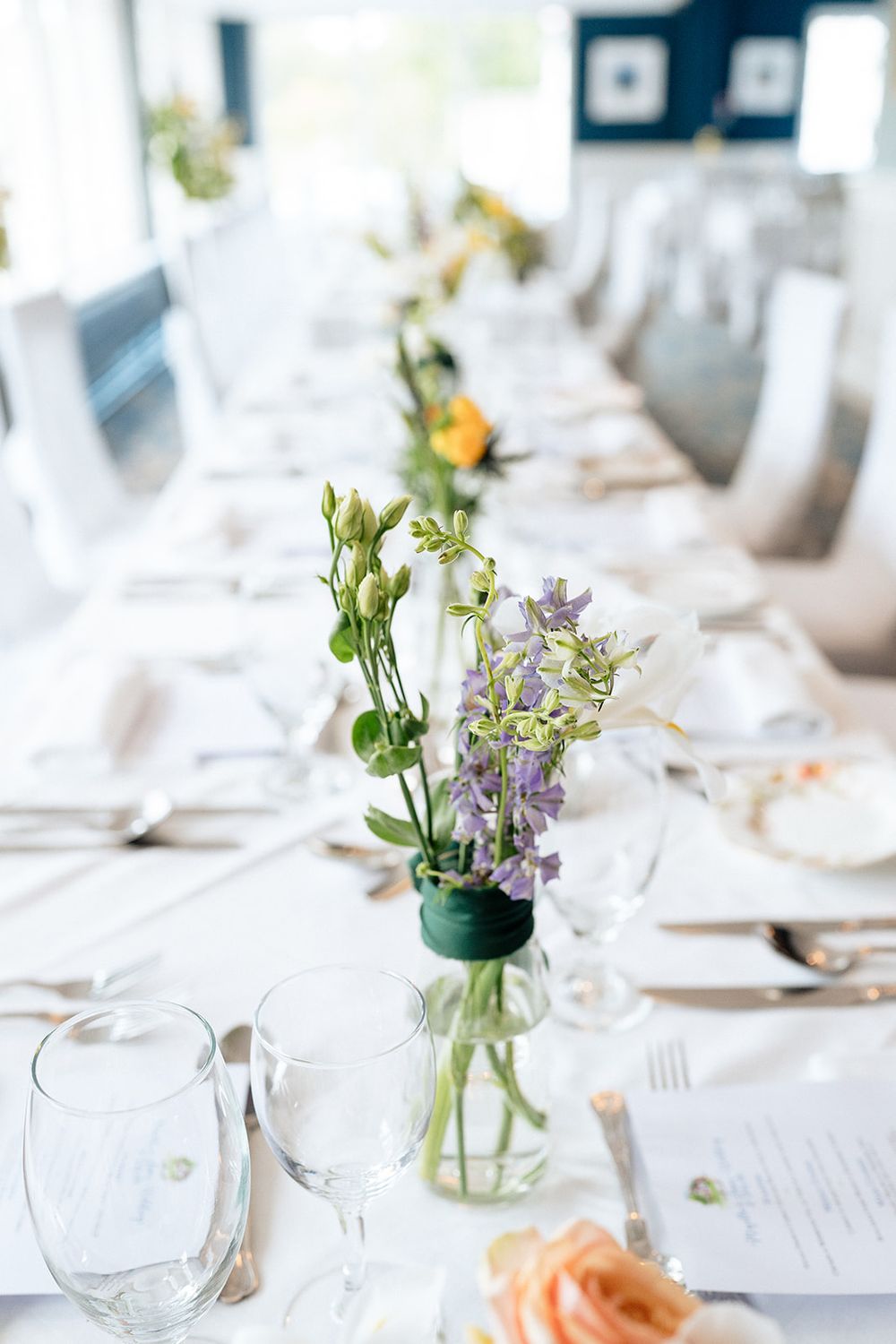 Elegant table settings at a wedding reception featuring delicate wildflower centerpieces in glass vases on white linens.