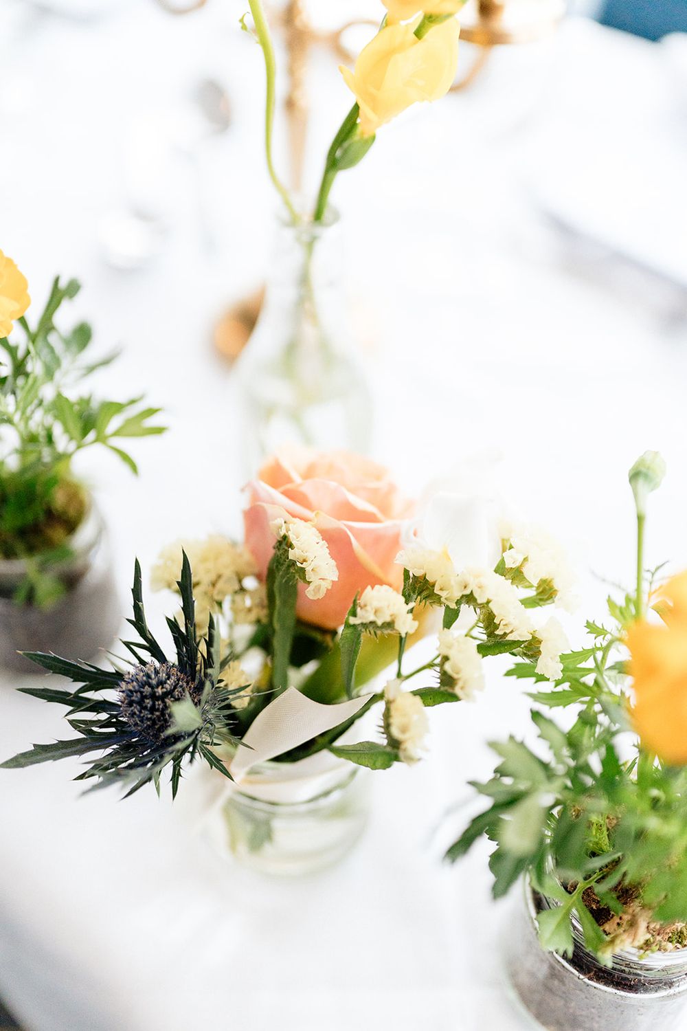Delicate floral arrangements in small white vases with pink and yellow blooms and green foliage against a white background.
