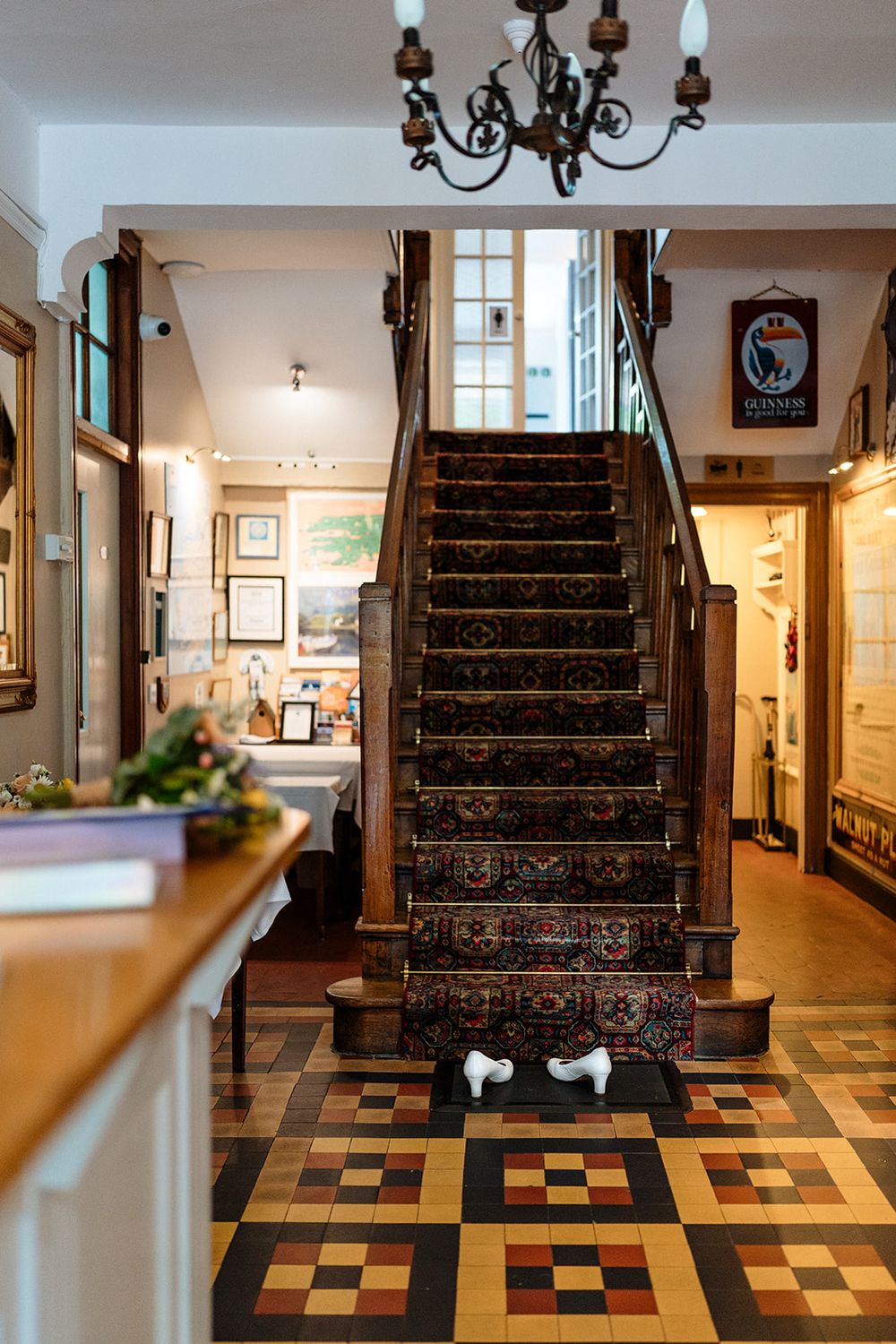 Elegant stairs with ornate carpeting and black wrought iron railing ascend above a checkered floor in a historic interior.