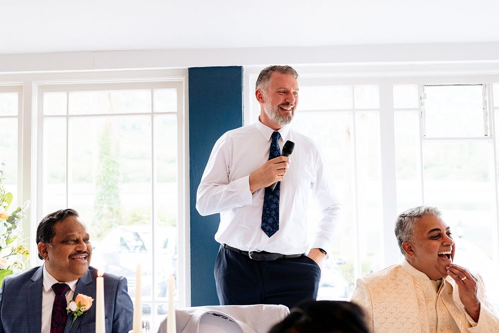 People enjoying a speech during a bright indoor celebration with natural light streaming through windows.
