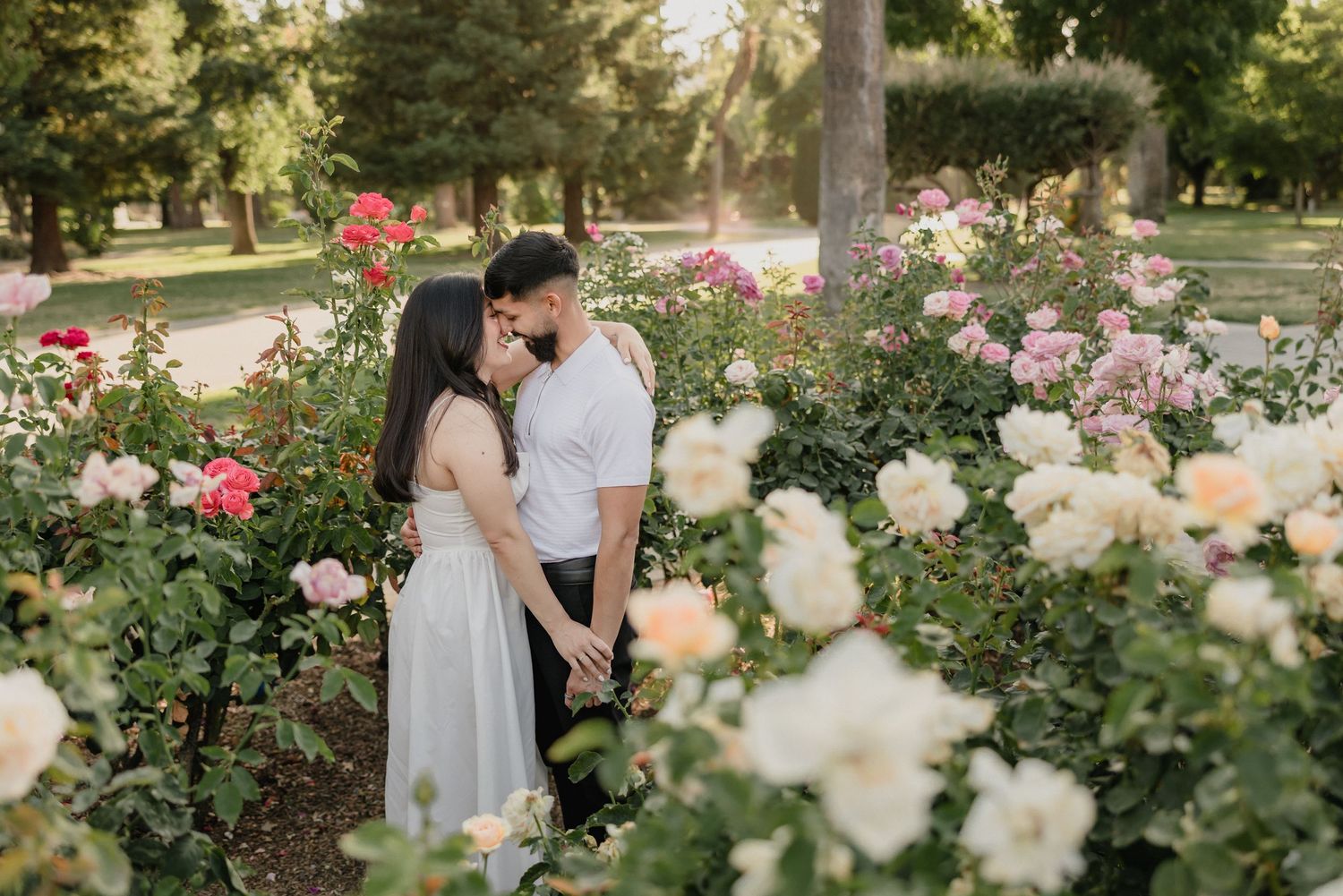 A romantic scene unfolds in a lush rose garden during golden hour as silhouettes stand among pink and white blooms.
