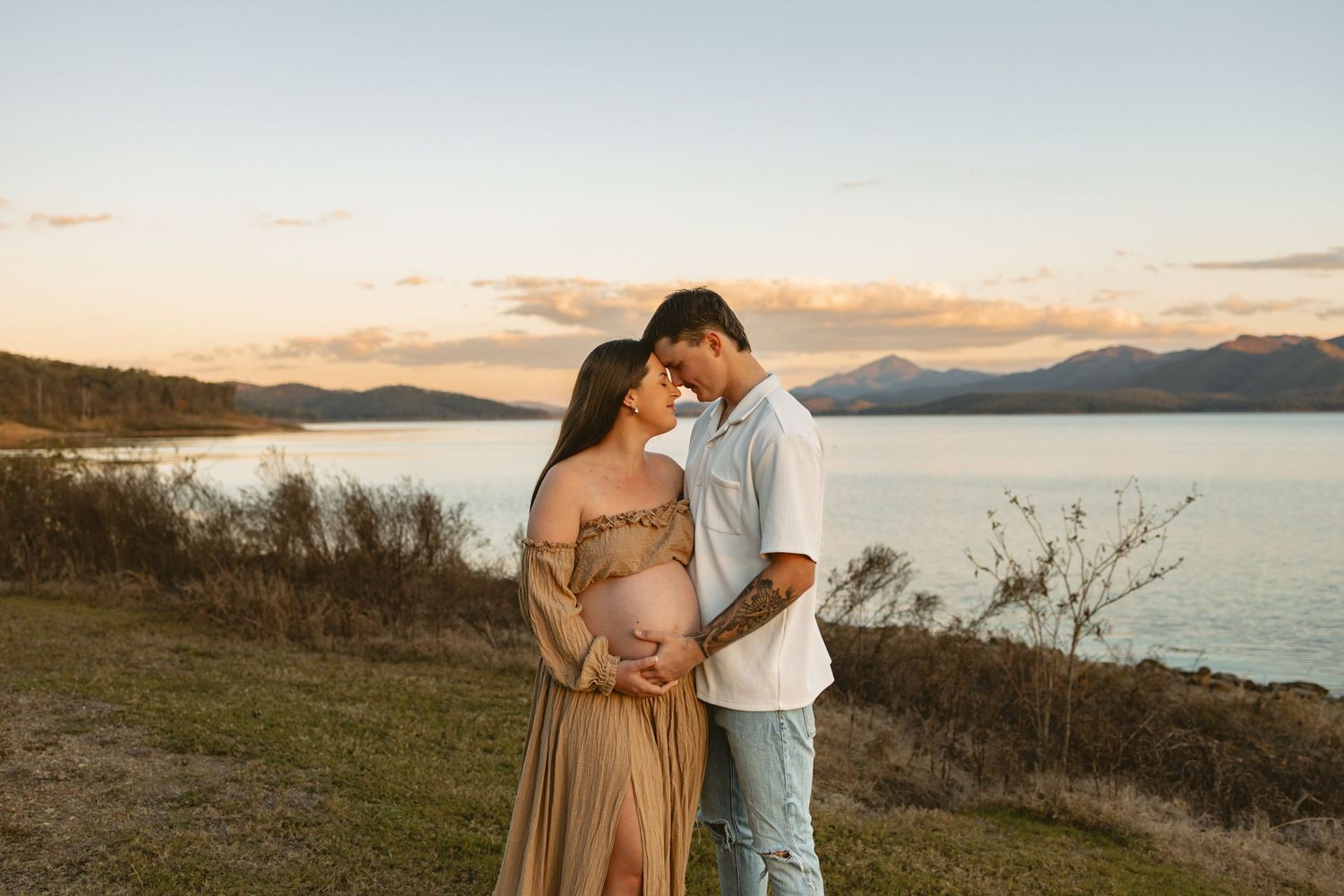 Couple embracing on a coastal overlook with mountains and water in the background during golden hour sunset.