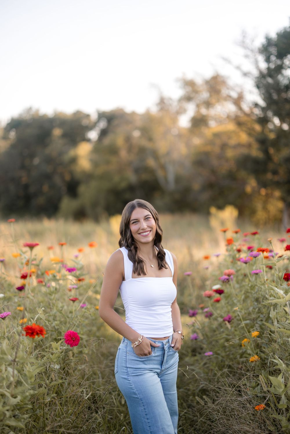 A figure stands among vibrant orange and pink zinnias in a wildflower meadow during golden hour.