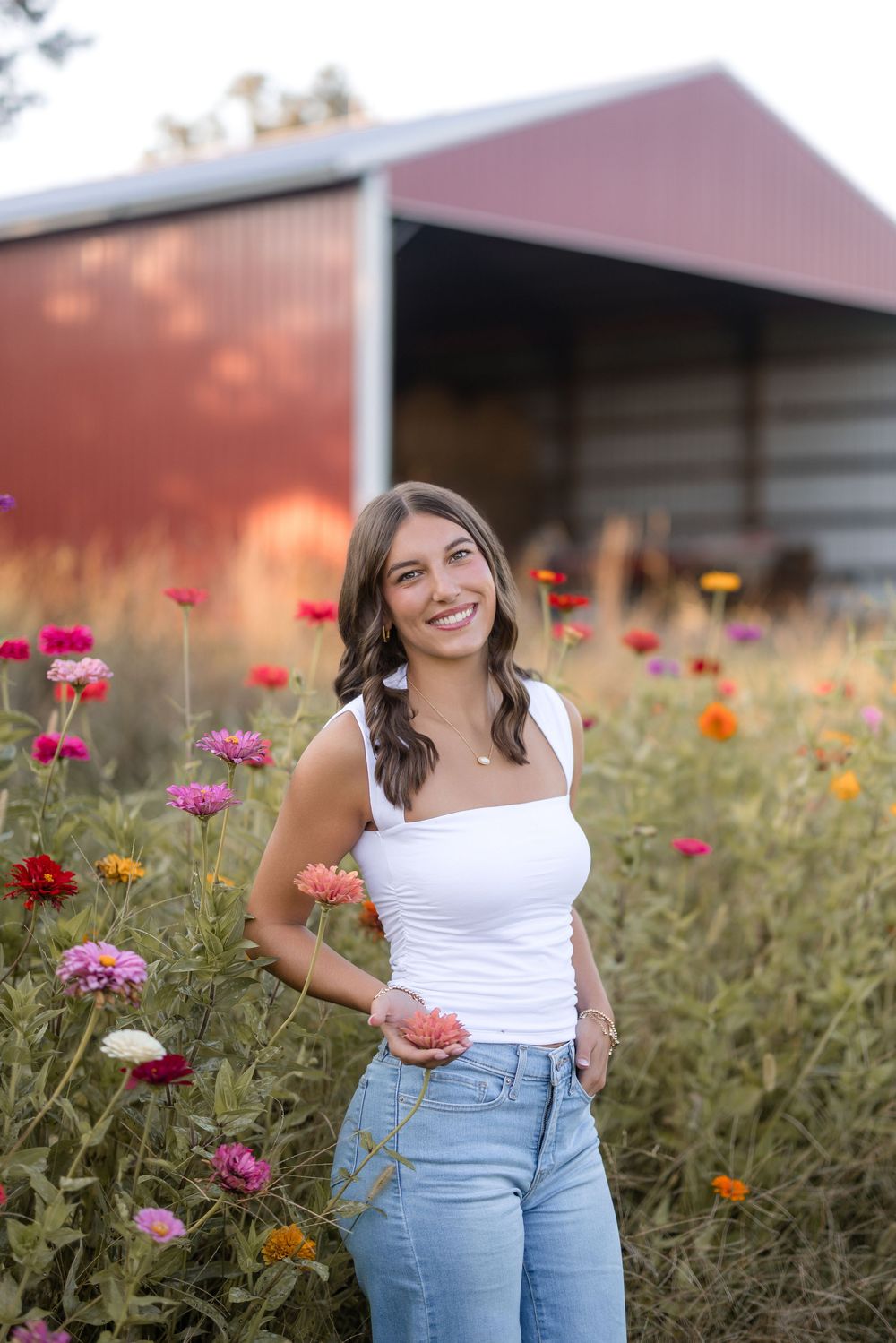 Someone in a white top and jeans poses in a garden filled with vibrant pink and orange wildflowers at sunset.