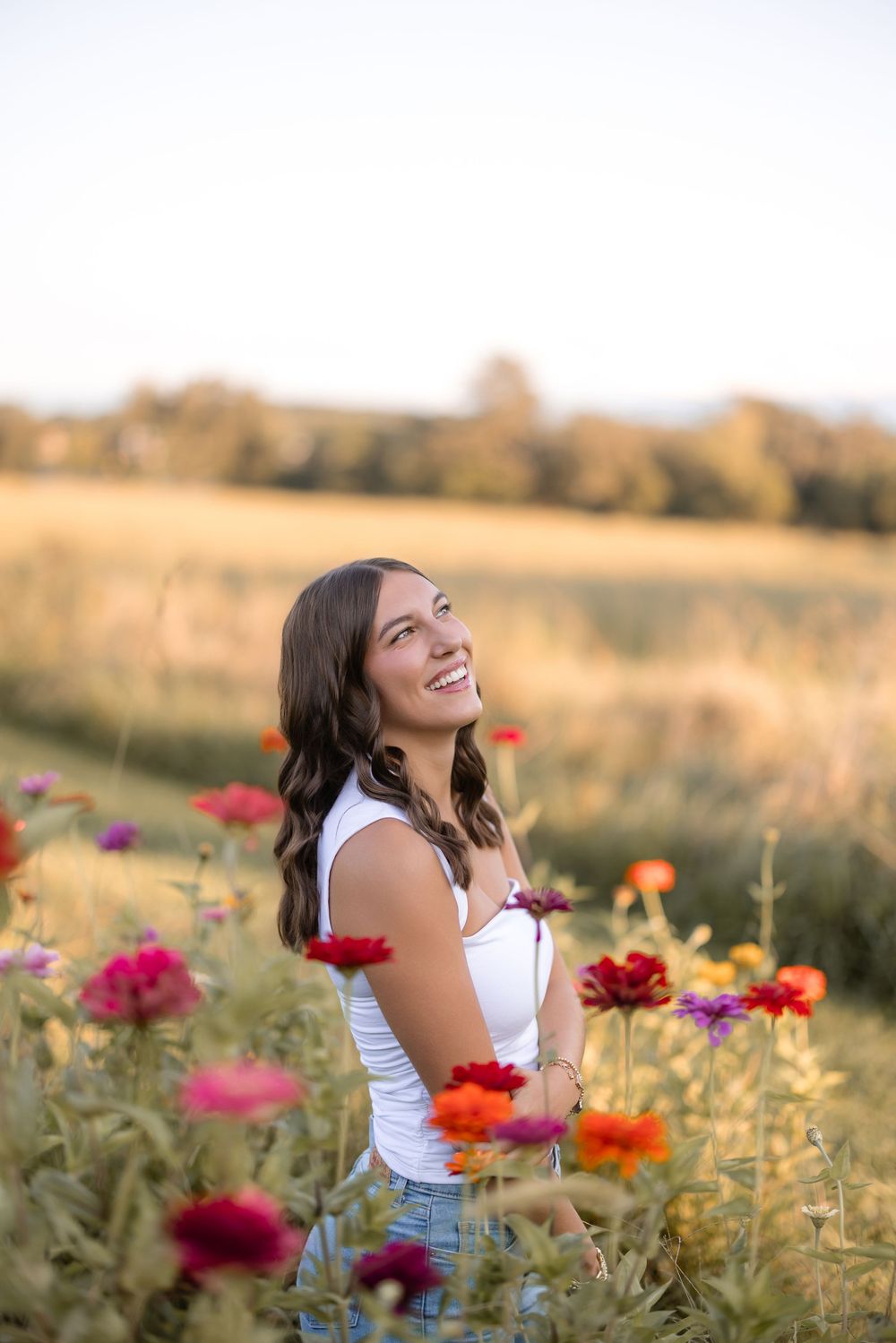 A woman laughs joyfully among colorful wildflowers in a golden summer field at sunset.