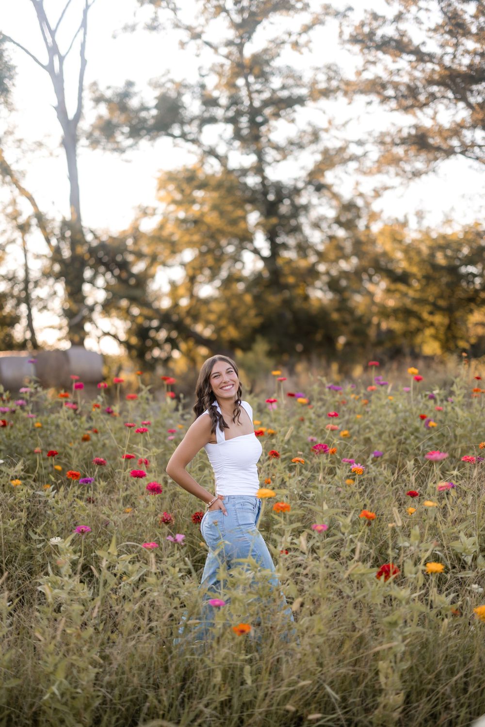A person in a white top and jeans poses gracefully in a vibrant wildflower field during golden hour.