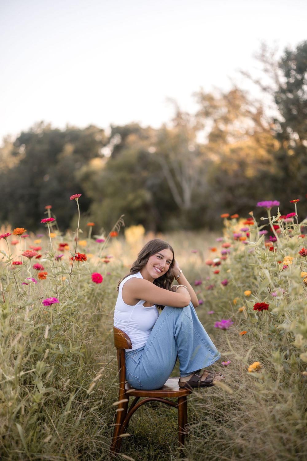 Person sits in vintage wooden chair among vibrant wildflowers at sunset in a meadow.