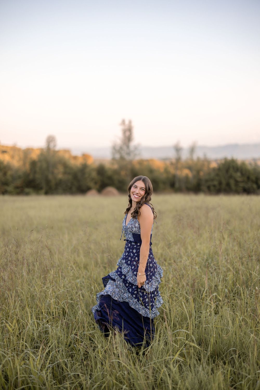 A dreamy sequence of someone in a navy polka dot dress walking through a golden grass meadow at sunset.