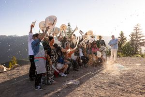 Group celebrating on a mountaintop at sunset with raised hands.